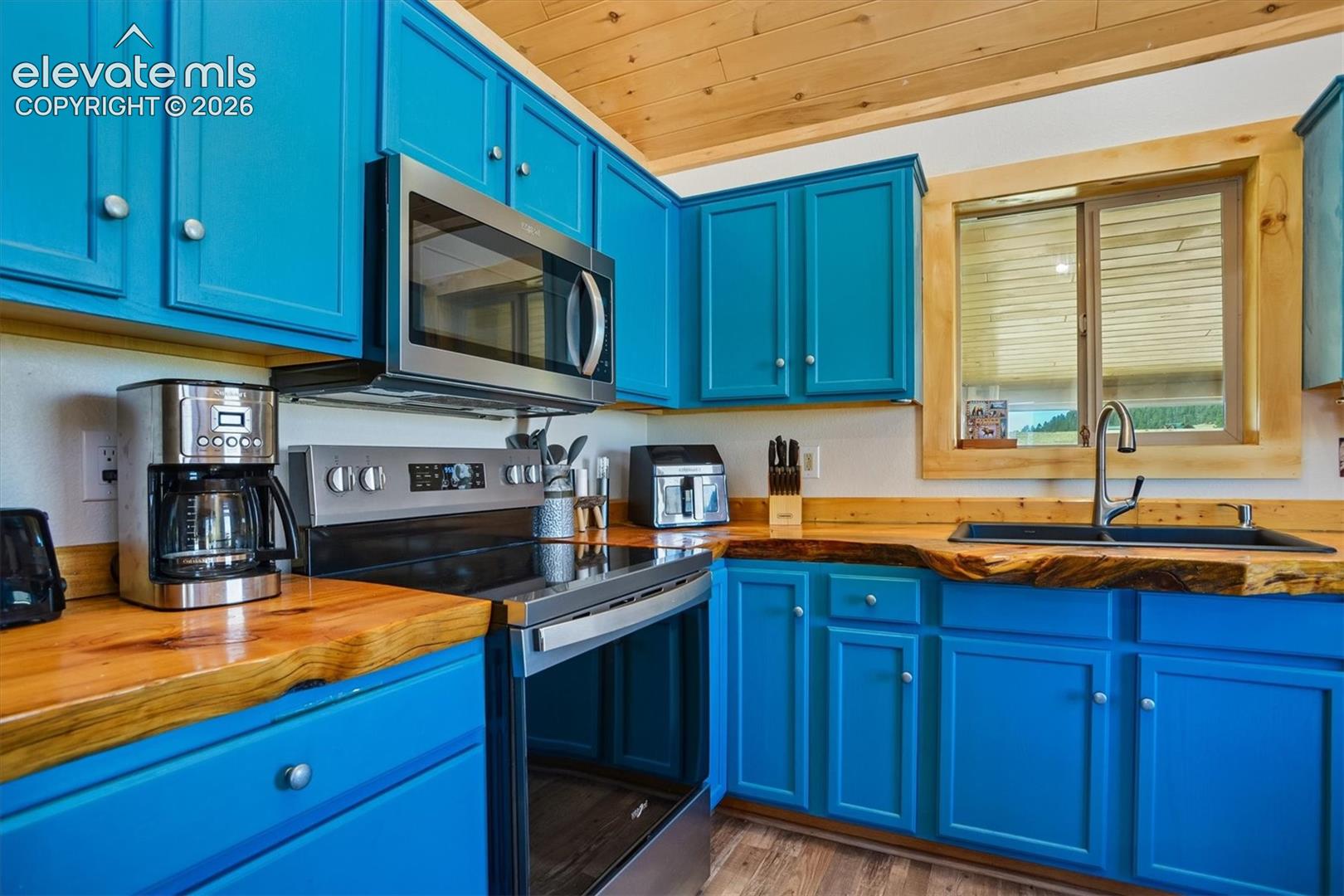 Kitchen showcasing vibrant blue cabinetry, live-edge wood countertops, and stainless steel appliances including an oven range and microwave