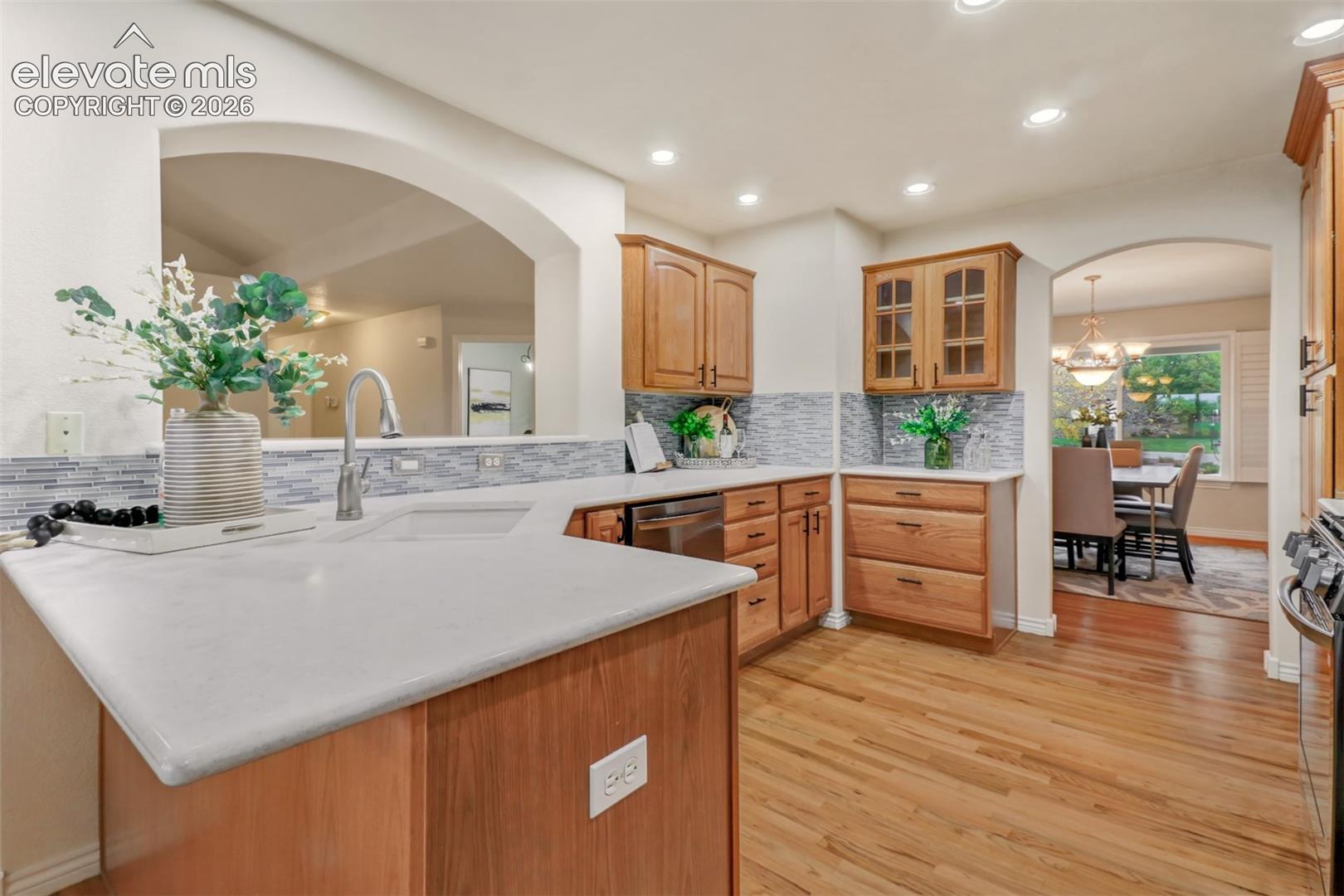 Kitchen featuring wood cabinetry, solid-surface countertops, mosaic tile backsplash, recessed lighting, and wood-finish flooring