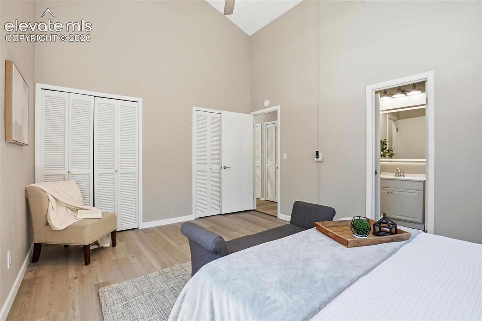 Spacious room featuring vaulted ceilings, wood-finish flooring, two sets of bi-fold louvered closet doors, and access to an en-suite bathroom with vanity lighting