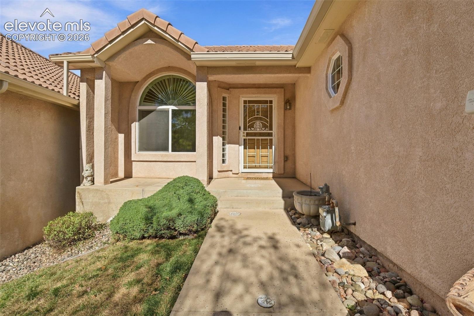 Stucco exterior featuring an arched window, decorative screen door, concrete entryway, and tile roof