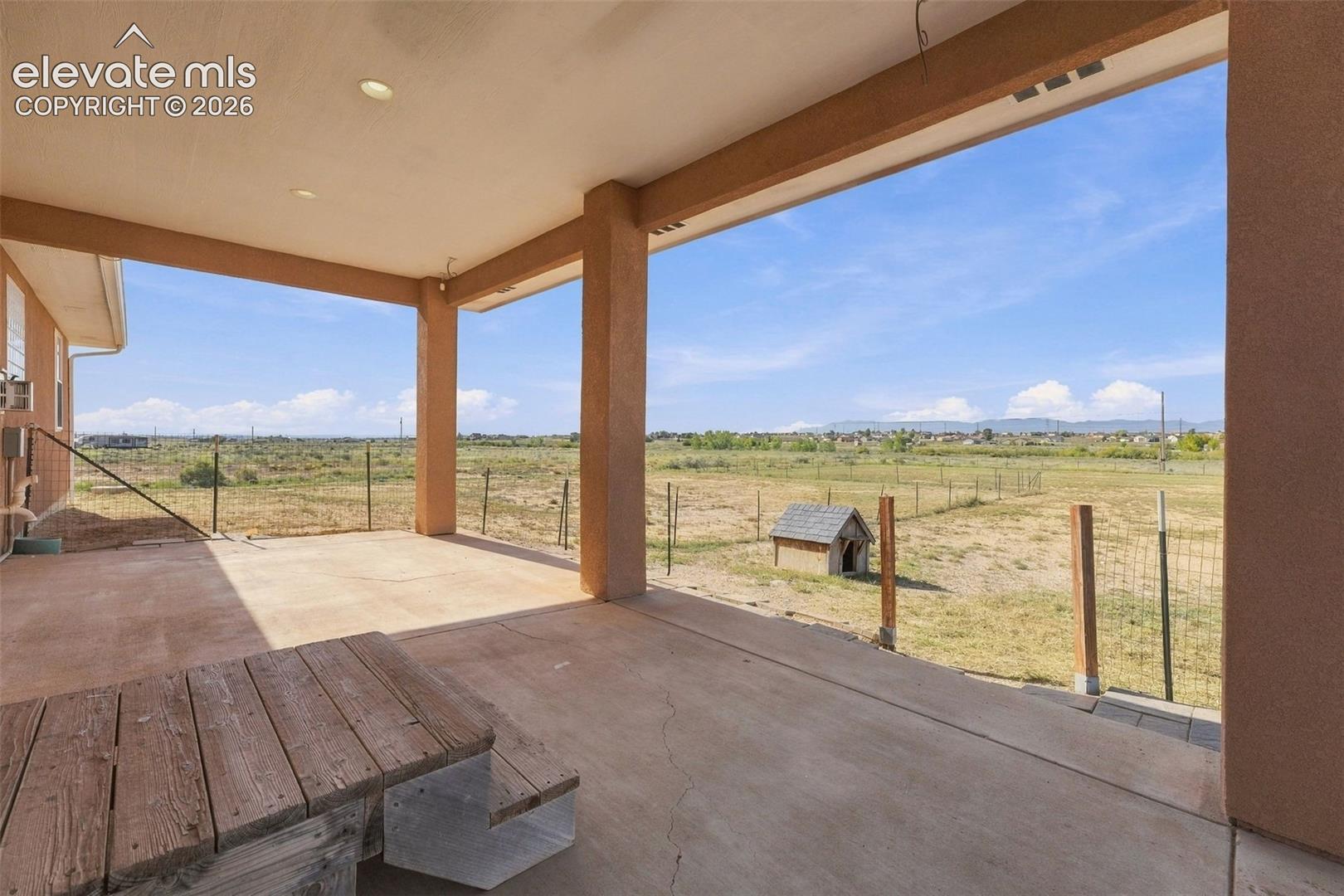 Covered concrete patio featuring recessed lighting, support columns, and an open, expansive outdoor area with perimeter fencing