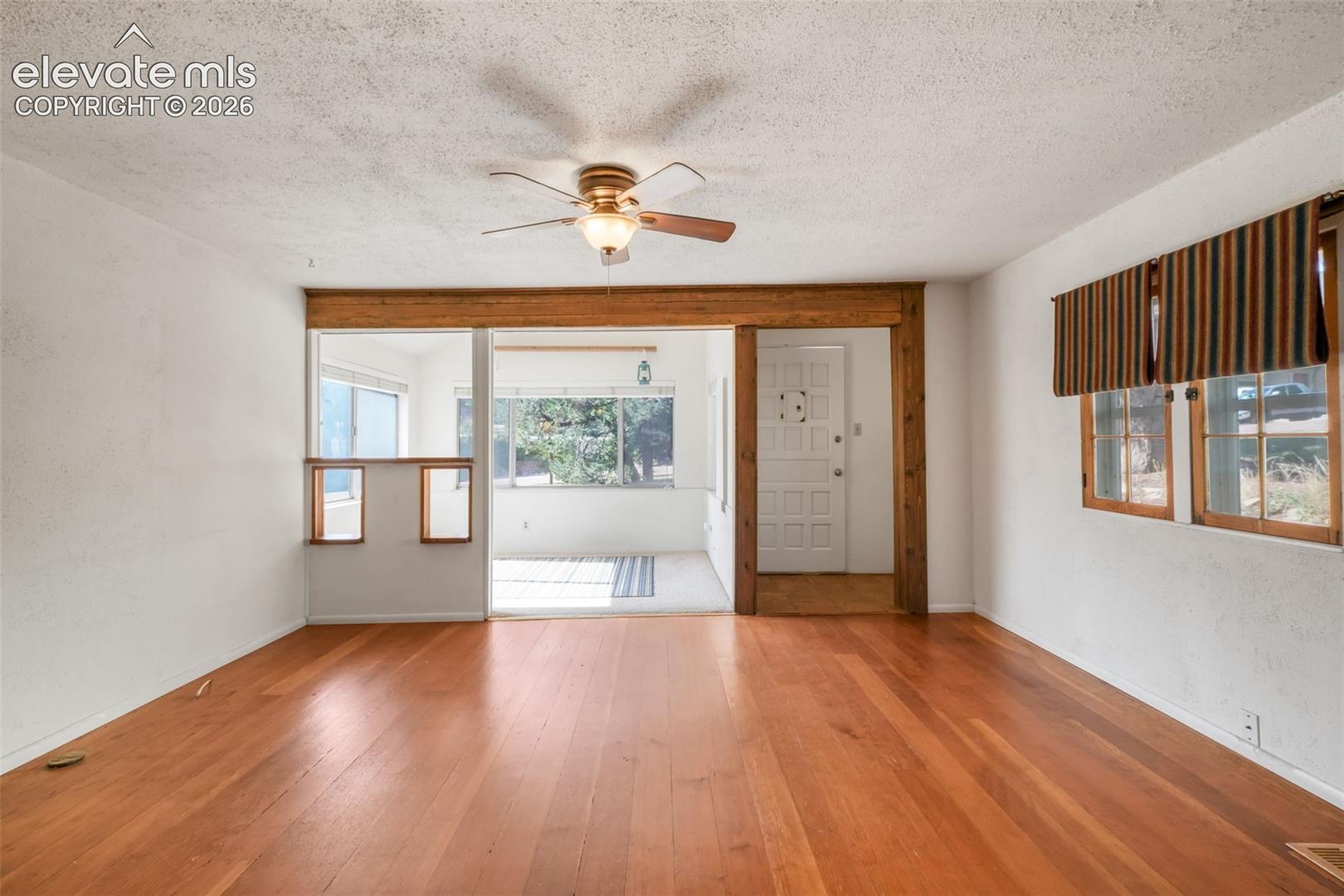 Wood-finish flooring throughout, ceiling fan with integrated lighting, wood-framed entry door, and a sunroom with expansive windows