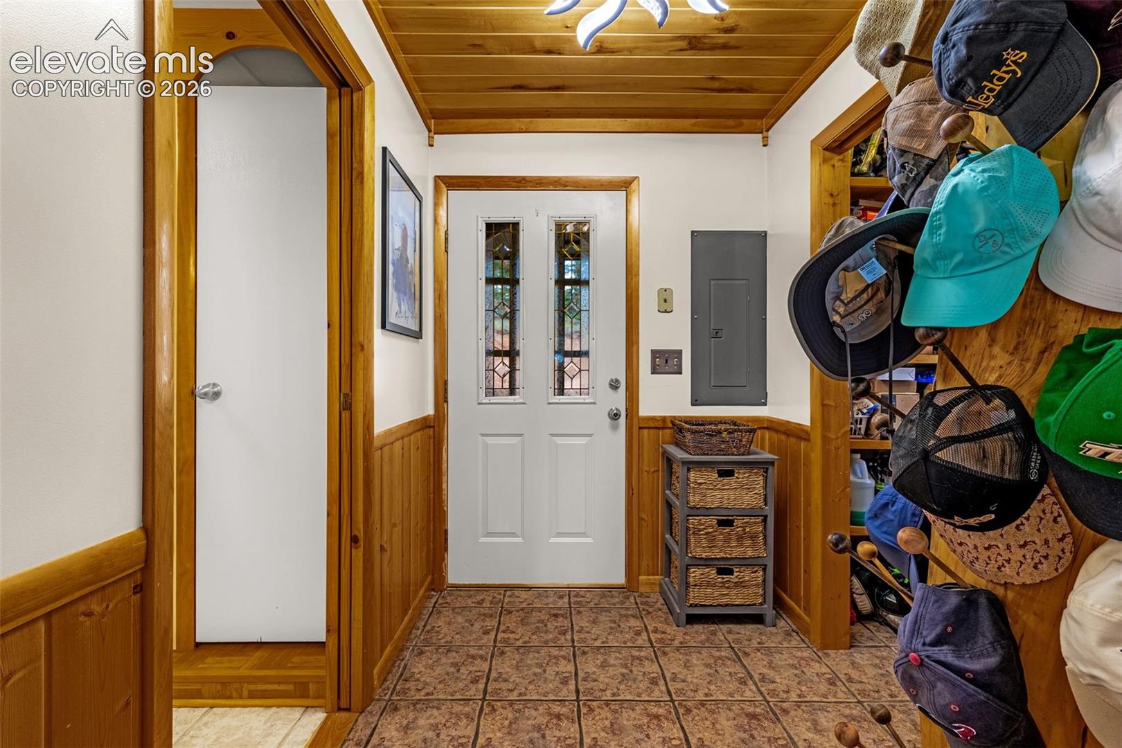 Entryway featuring natural wood-plank ceiling, wood wainscoting, tiled flooring, and an exterior door with decorative leaded glass inserts