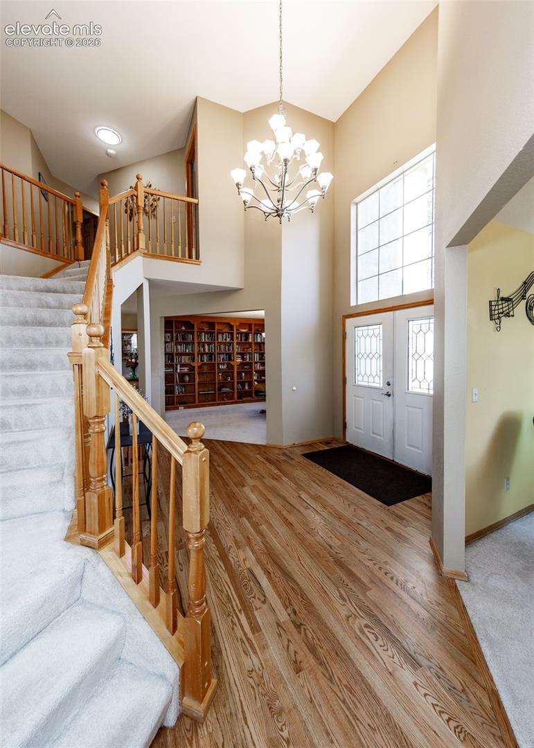 Two-story foyer with vaulted ceiling, wood-finish flooring, staircase with wood newel posts, and a decorative chandelier