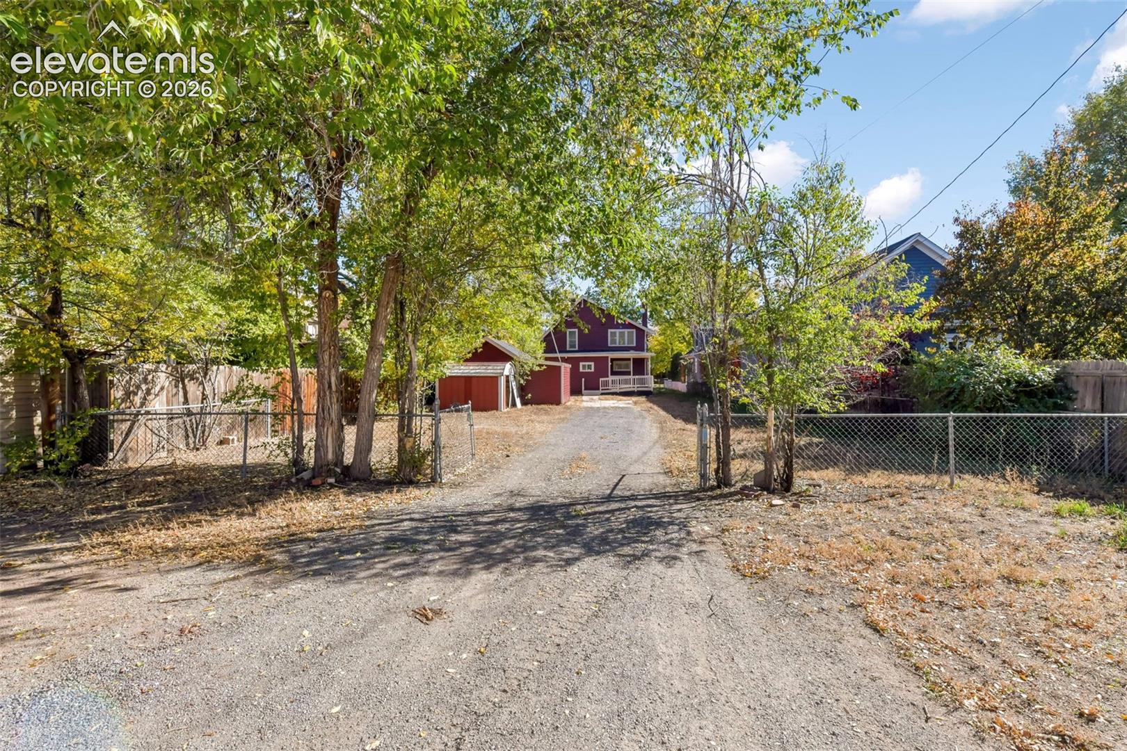 Gravel driveway leading to a detached structure, mature trees, and fenced perimeter