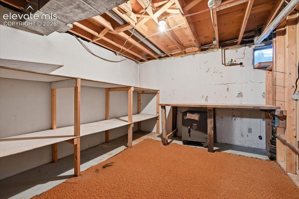 Lower level utility space featuring built-in wooden shelving, exposed timber ceiling joists, and a stationary wooden workbench
