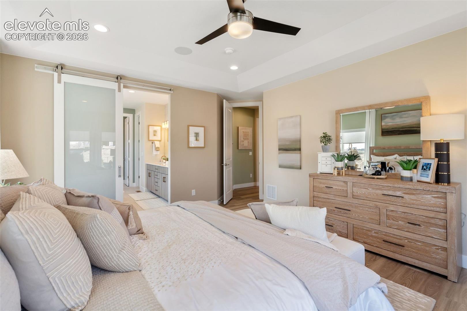 Tray ceiling with recessed lighting, ceiling fan with integrated light fixture, and frosted glass sliding door with stainless steel hardware