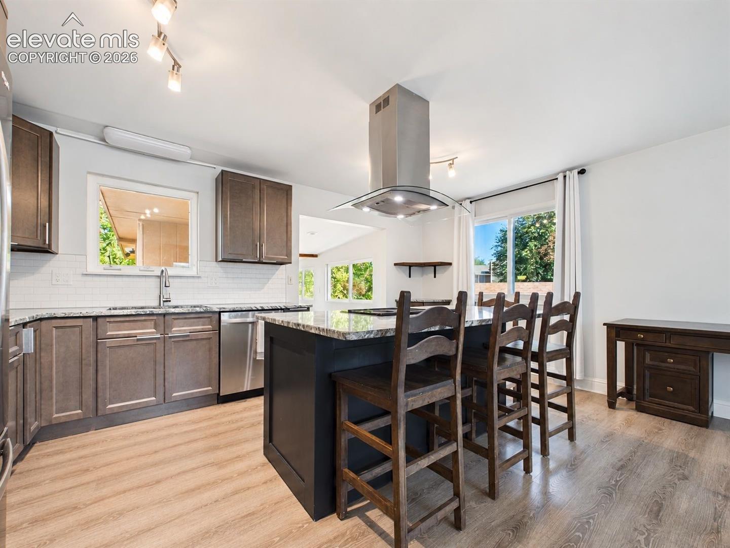 Wide view captures the remodeled kitchen's large island, seating area, stainless steel appliances, and convenient connection to the window-lined sunroom.