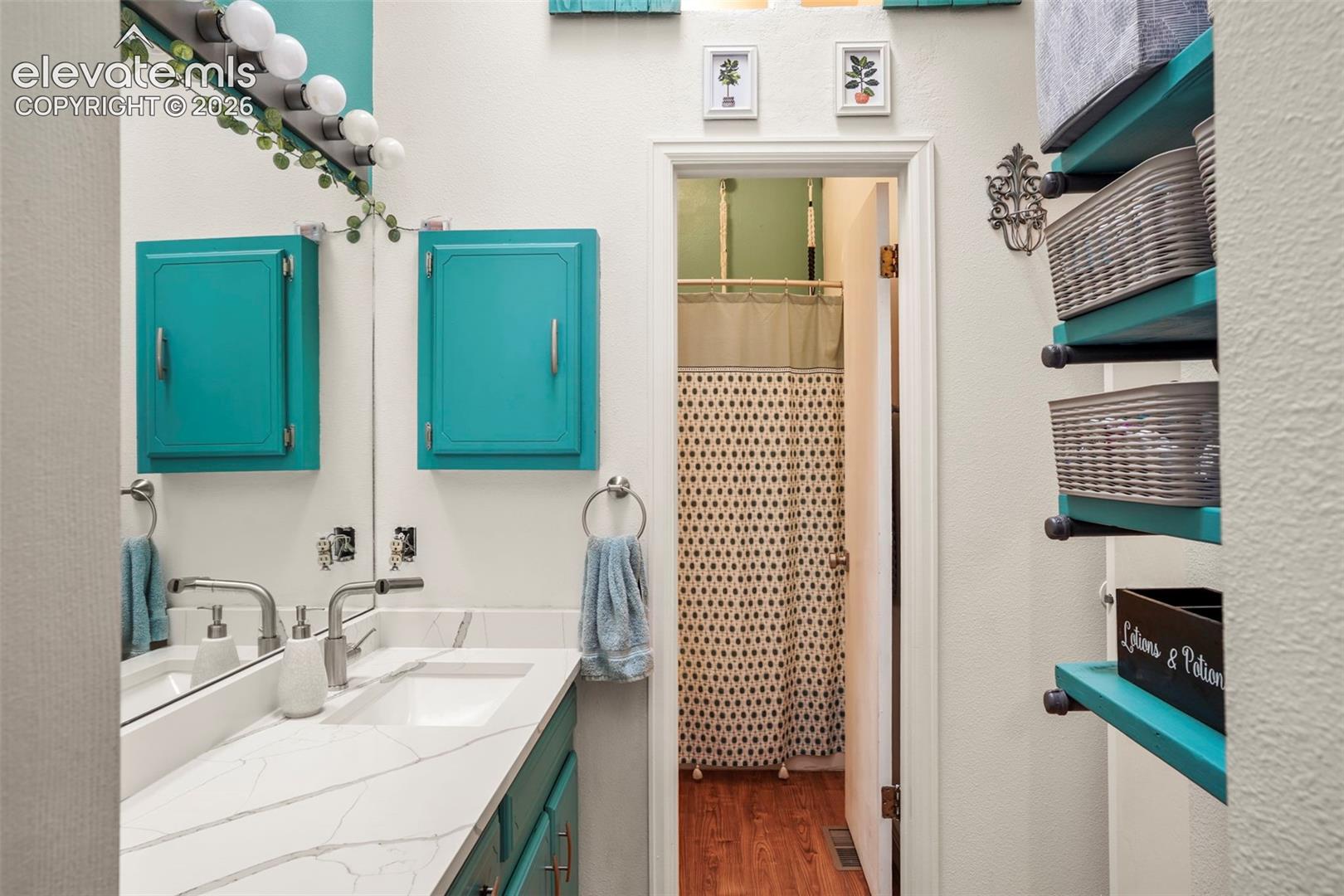 Bathroom featuring a white countertop with veining, rectangular integrated sink, wall-mounted brushed metal faucet, vanity with teal cabinetry, and industrial-style open shelving with pipe supports