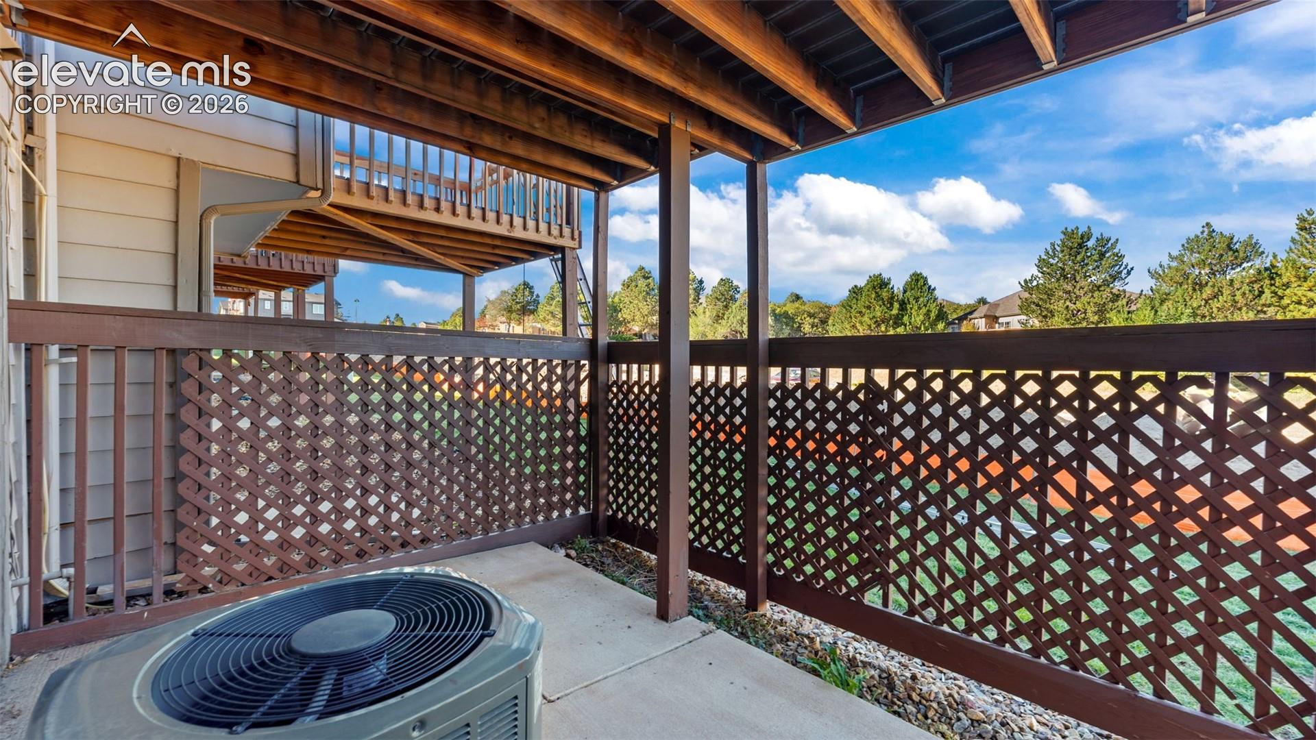 Covered ground-level patio with concrete flooring, wood lattice privacy fencing, and exposed wood support beams