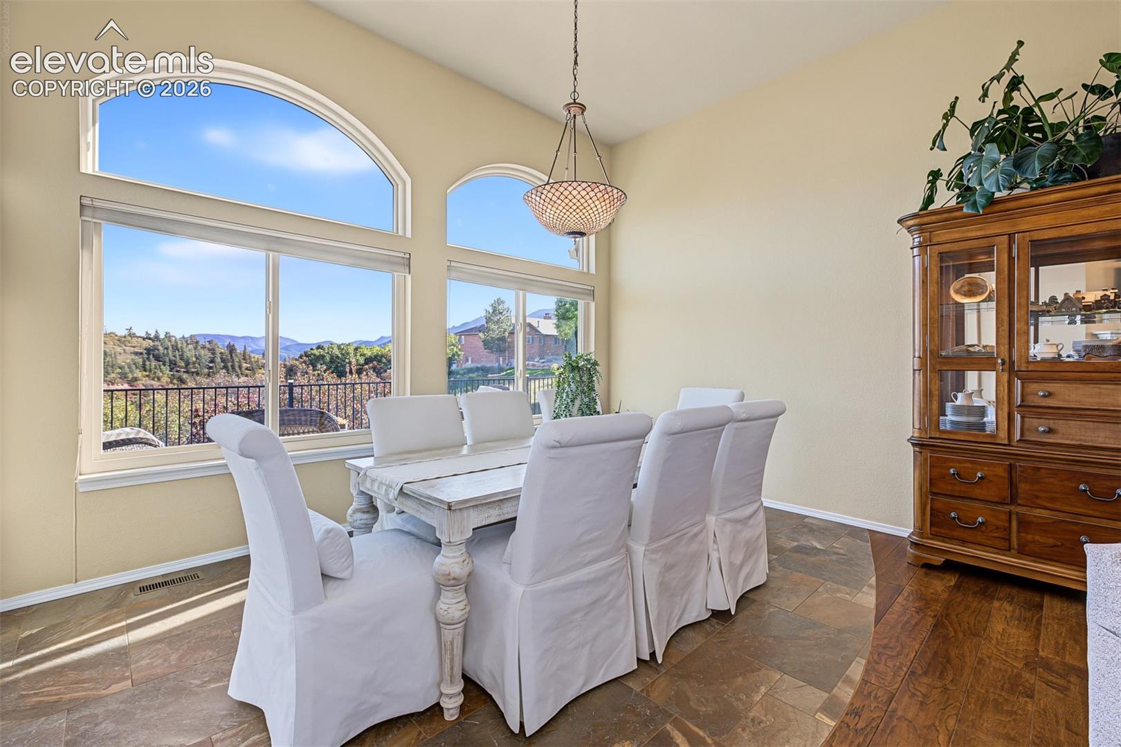 Dining area featuring expansive windows with arched transoms, mountain views, views of the rear deck, a decorative chandelier, and tile flooring.