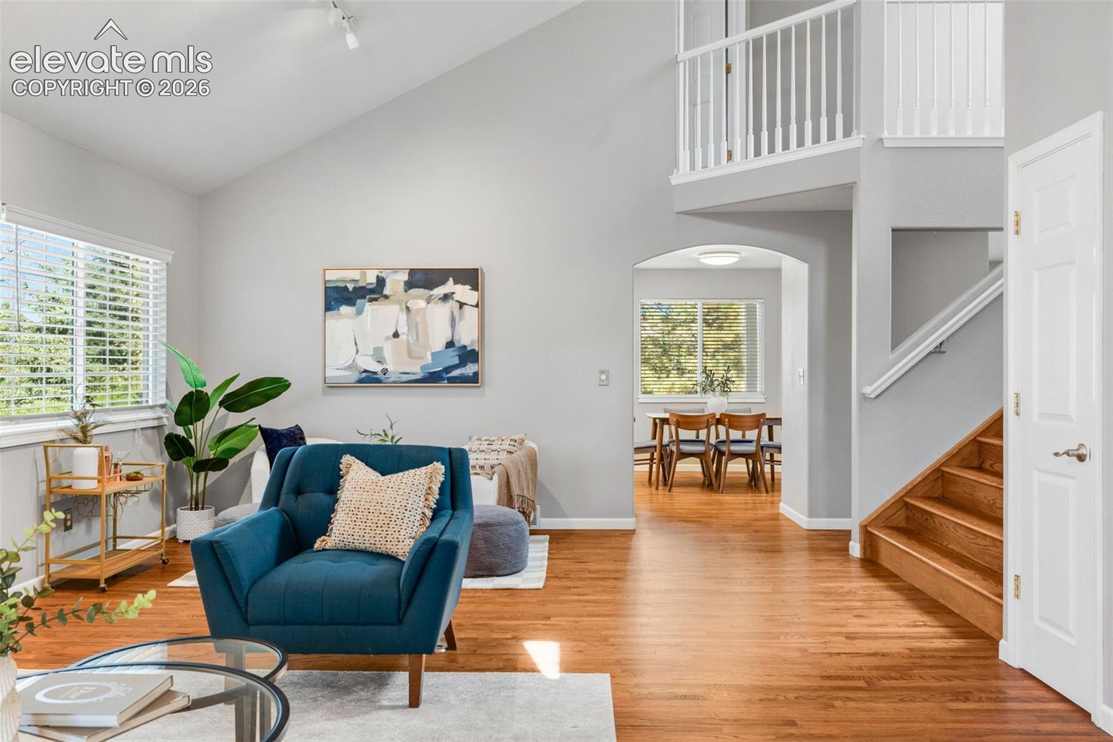 Vaulted ceilings, wood-finish flooring, an arched entryway, and a staircase with a white spindle railing