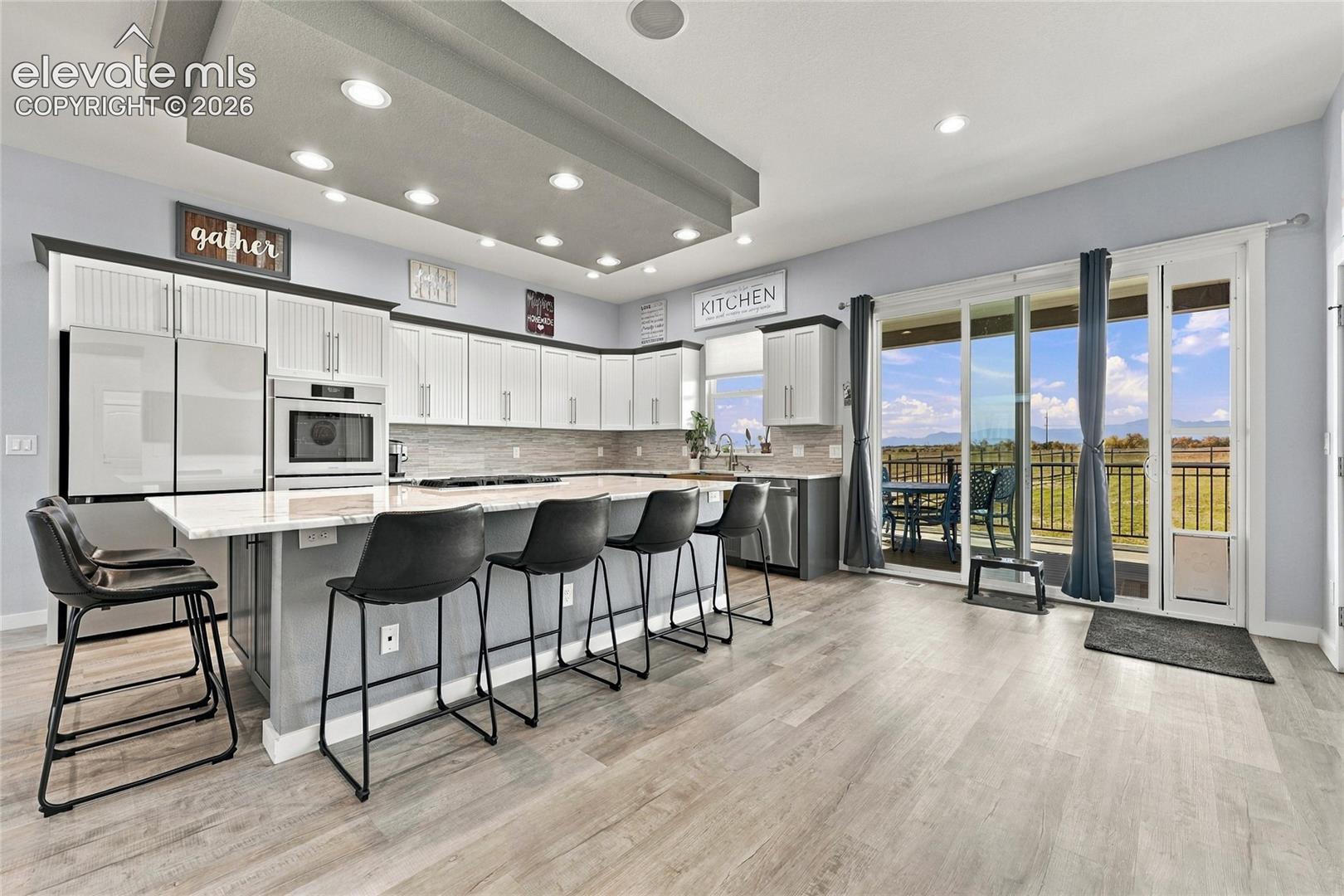Kitchen featuring white cabinetry, an expansive island with stone-finish countertops, built-in stainless steel appliances, recessed ceiling lighting, and sliding glass doors