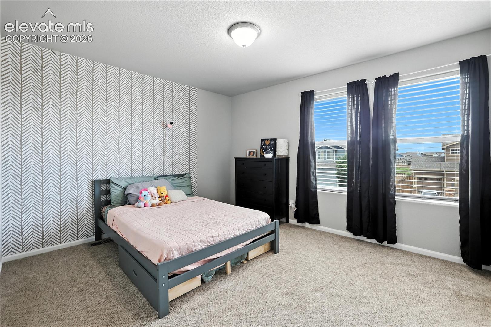 Accent wall with geometric wallpaper, wall-to-wall carpeting, and three windows with blinds