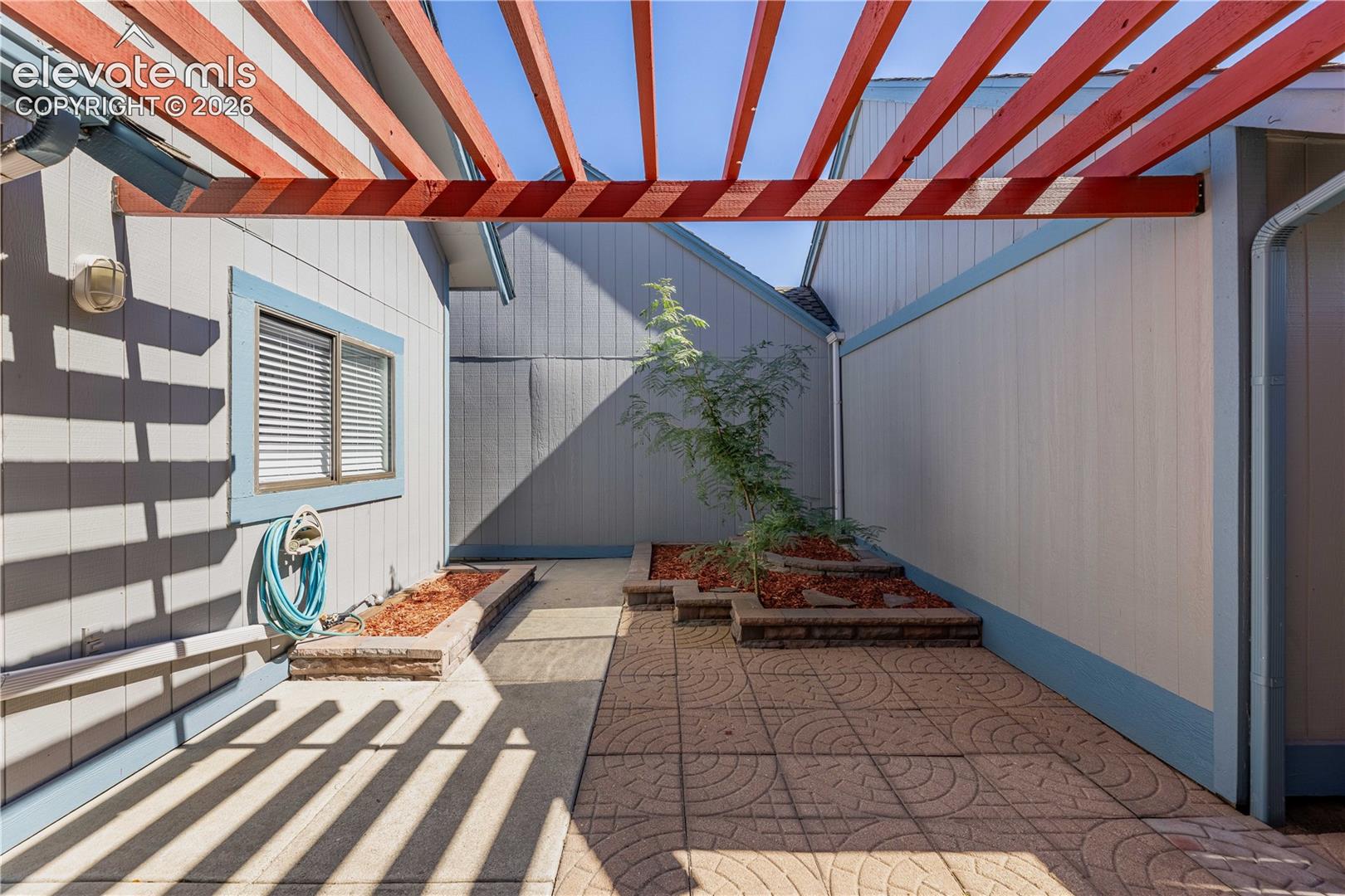 Private courtyard featuring a wood-beam pergola, stamped concrete patio, and tiered stone planters