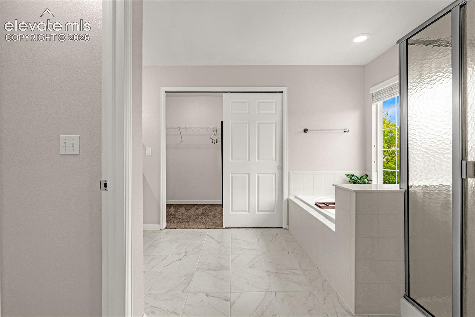 Bathroom featuring tiled flooring, a built-in soaking tub with a tiled surround, a glass-enclosed shower, and a walk-in closet with a panel door