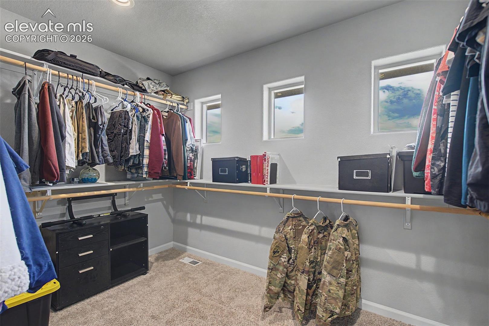 Walk-in closet featuring built-in shelving, multiple hanging rods, recessed ceiling lighting, and three transom windows