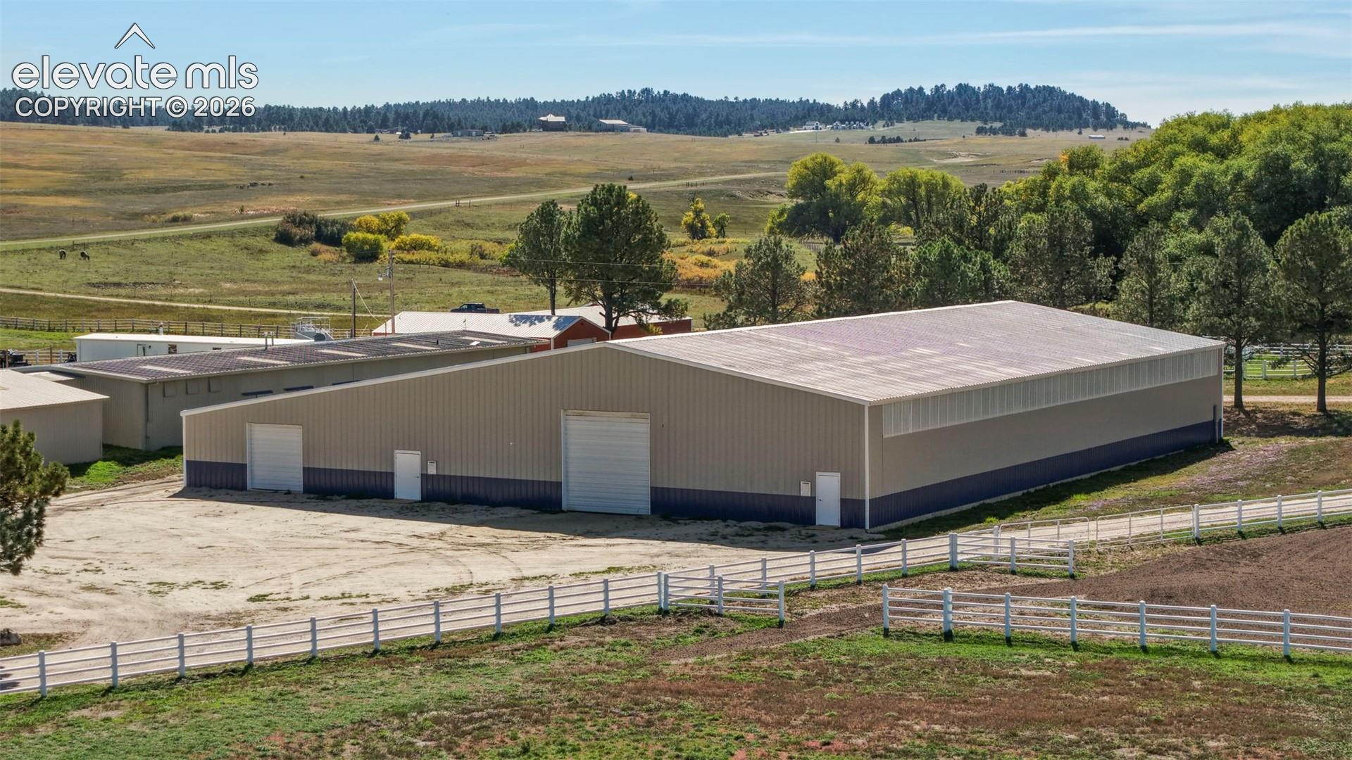 Arena - Large metal building with multiple access doors, a wide garage door, and a white fence bordering the property