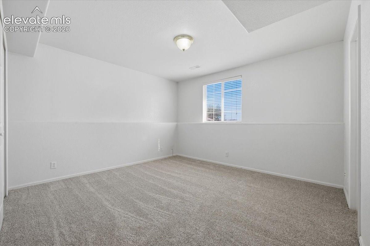 Wall-to-wall carpeting, overhead light fixture, window with blinds, and white painted walls