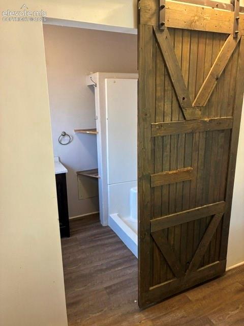 Bathroom featuring a sliding barn door with dark hardware, wood-finish flooring, a white shower enclosure, a vanity with a dark base, and a wall-mounted towel ring
