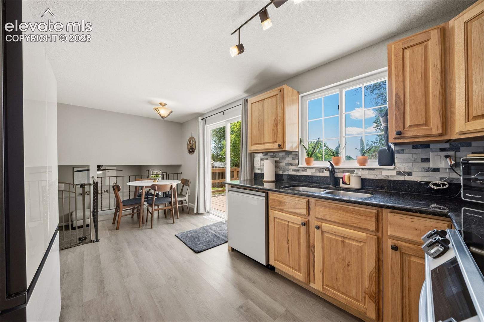 Kitchen featuring wood cabinetry, dark countertops, a tile backsplash, and wood-finish flooring