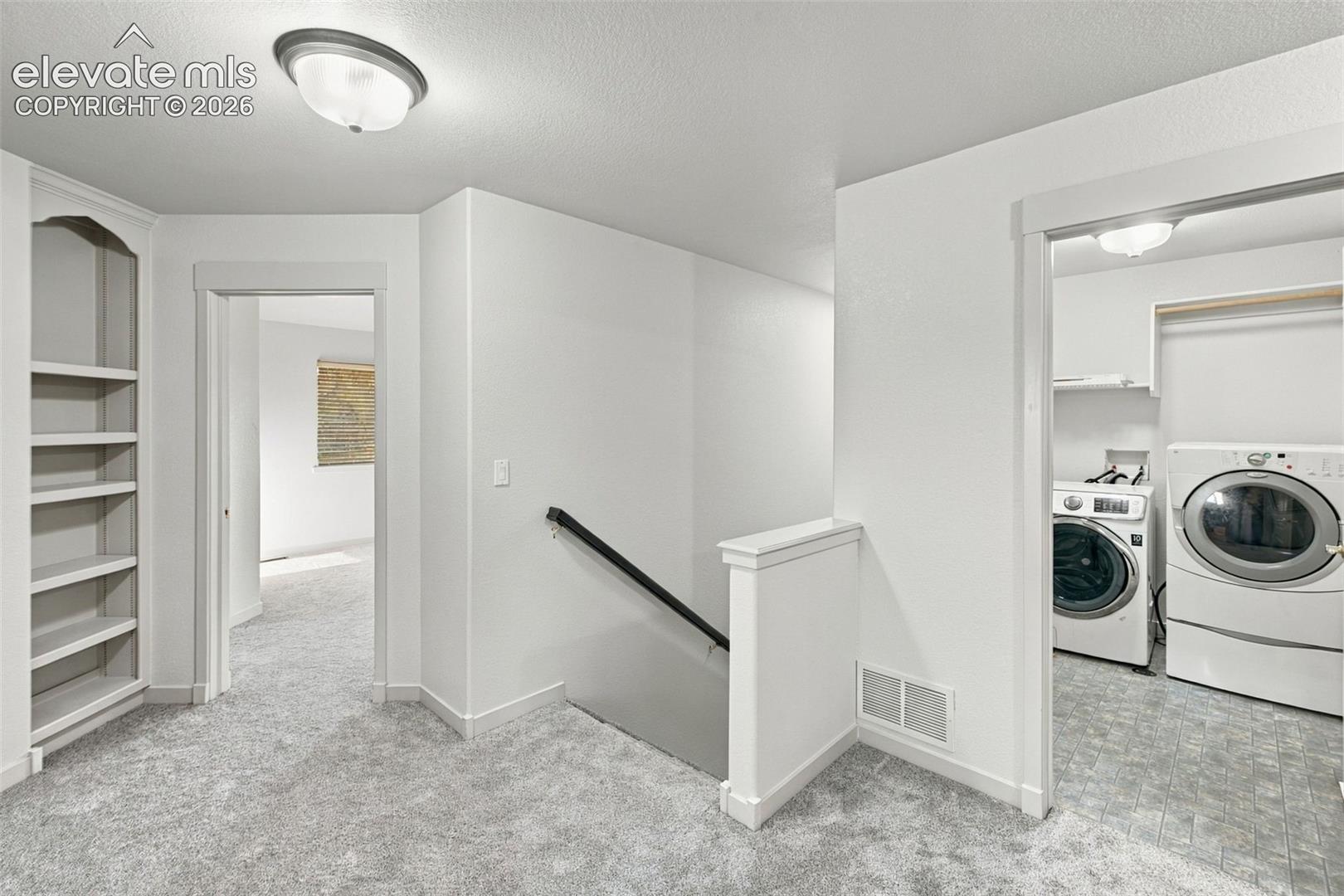 Built-in arched shelving, carpeted flooring, staircase with a handrail, and a dedicated laundry area featuring shelving and cabinetry