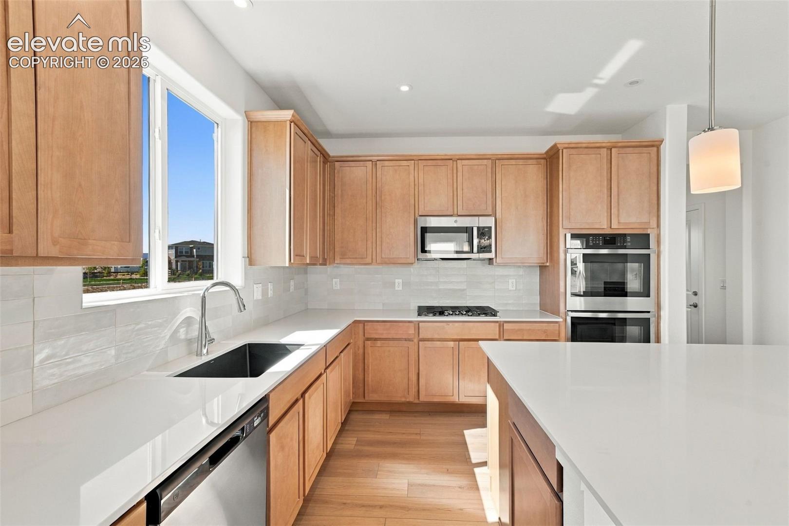 Kitchen featuring light wood-finish cabinetry, white countertops, stainless steel appliances, and a tile backsplash