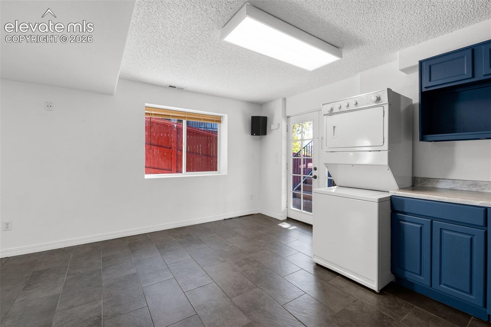 Tile flooring, white walls, built-in blue cabinetry, white stackable washer and dryer, and a glass-paned door