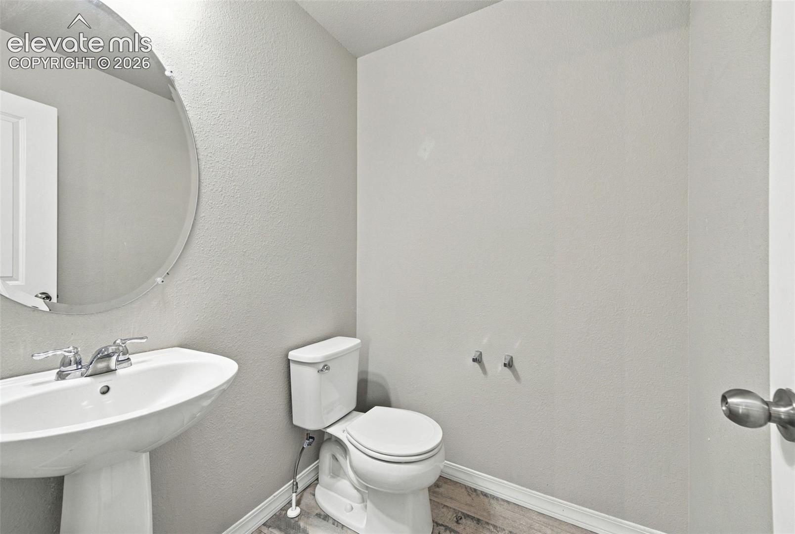 Powder room featuring a pedestal sink, dual-handle chrome faucet, round frameless mirror, and a porcelain toilet