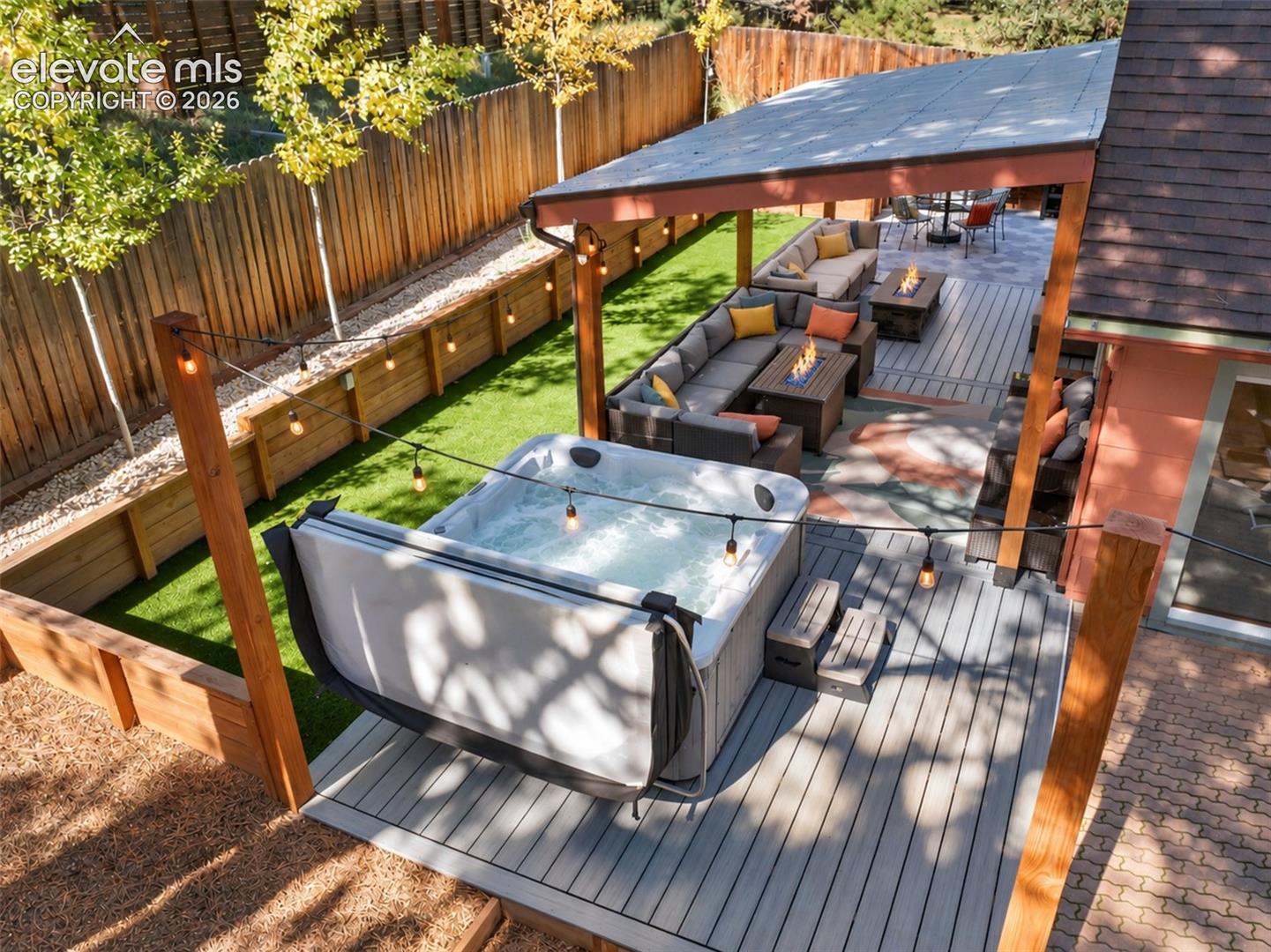 Outdoor living area featuring a covered deck, hardscaping, synthetic turf lawn, built-in hot tub, and wood privacy fencing