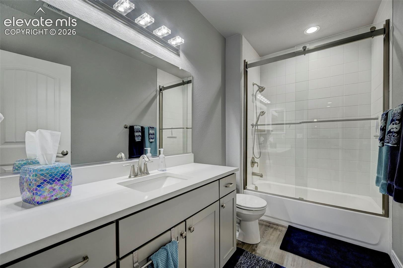Bathroom featuring a vanity with an integrated sink, a large mirror, and a shower-tub combination with a sliding glass enclosure