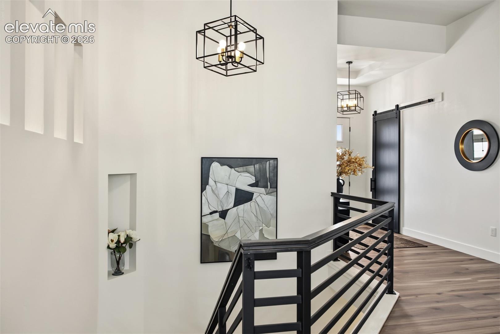 Bright, open hallway featuring elegant chandelier lighting, modern black iron railings, and an airy design overlooking the main level.