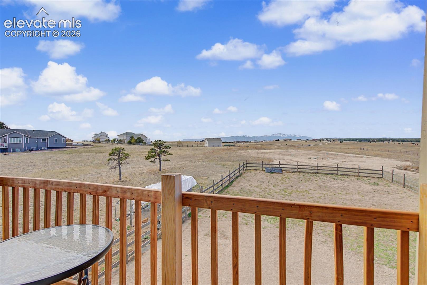Wood-railing balcony overlooking an expansive lot with post-and-rail perimeter fencing and a distant mountain backdrop