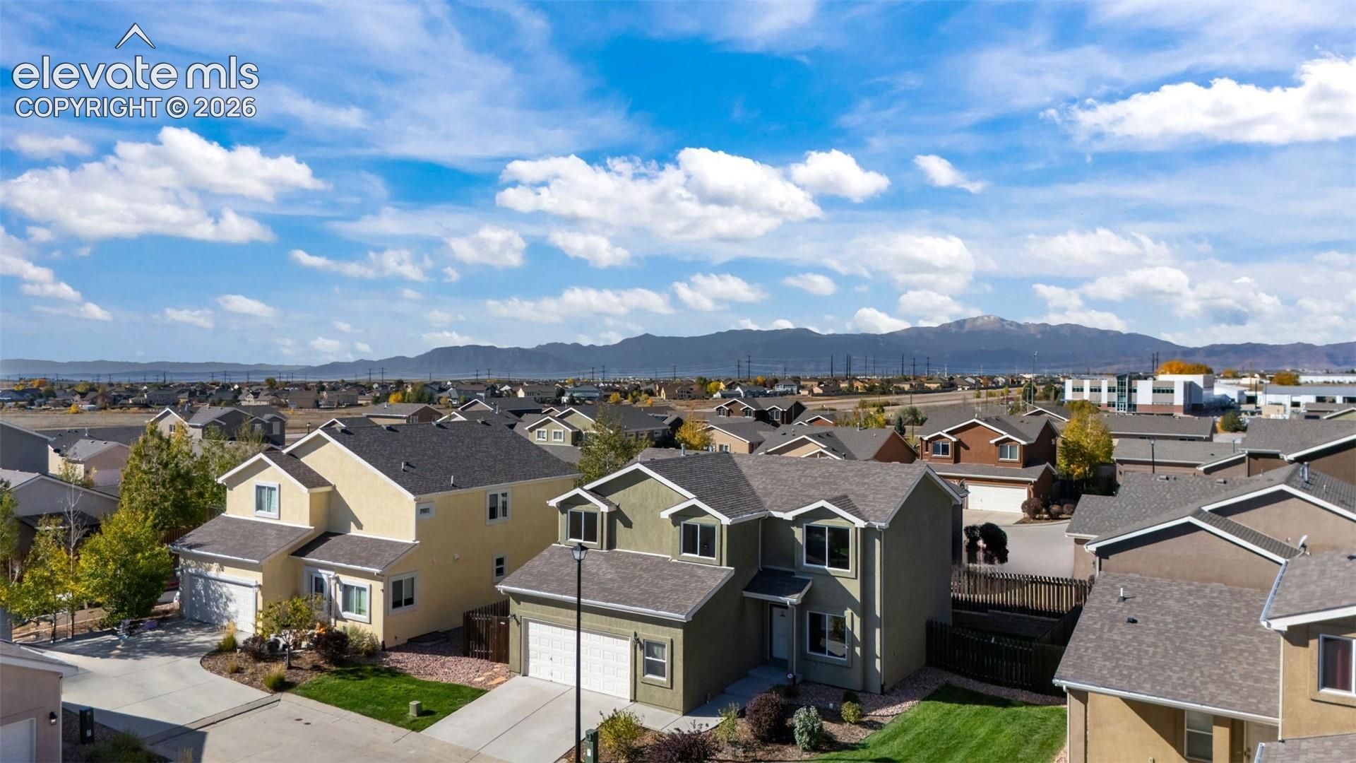 Aerial perspective showcasing multi-level residential architecture, asphalt shingle roofing, attached two-car garages, concrete driveways, and mountain backdrop
