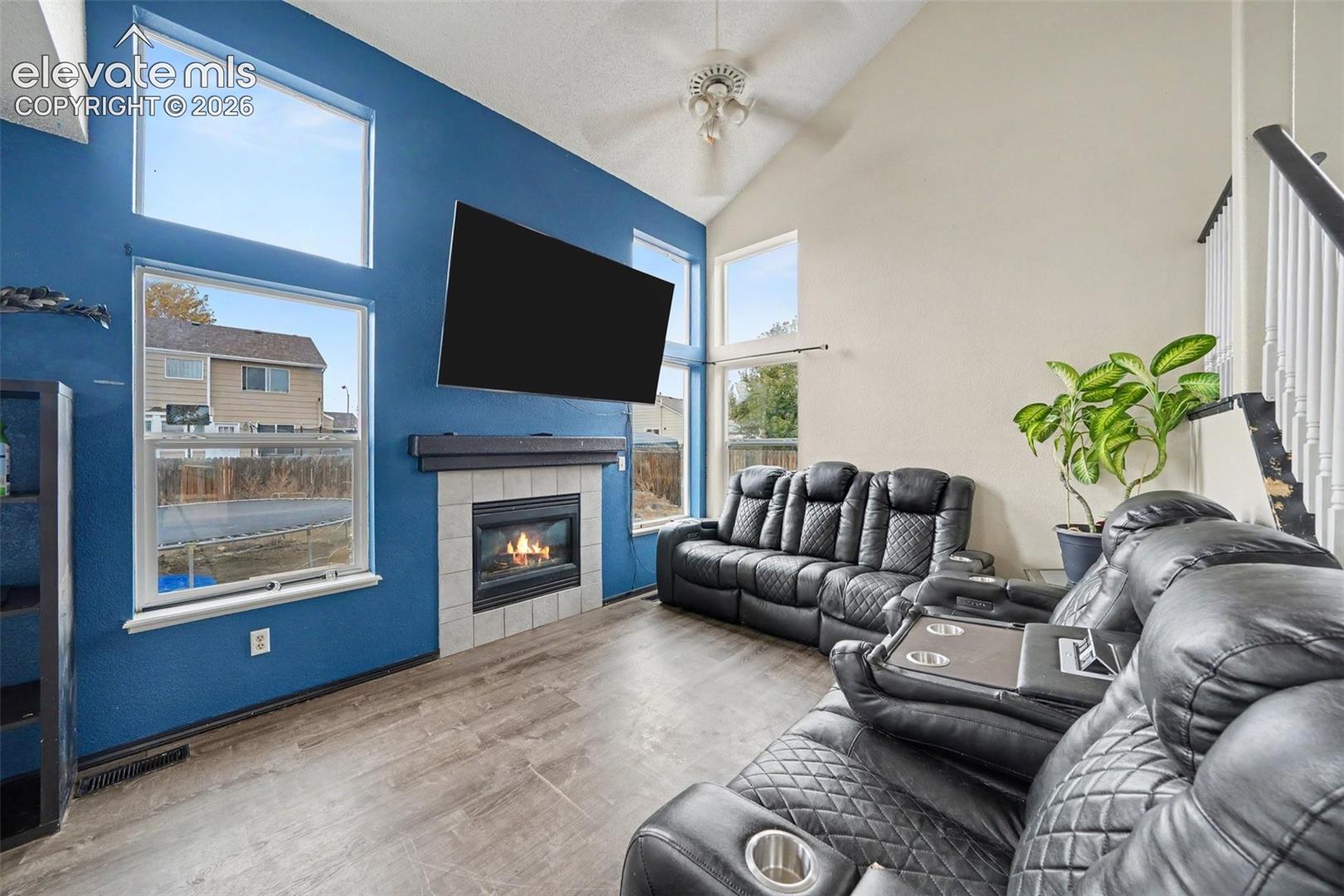 Vaulted ceilings, floor-to-ceiling windows, wood-finish flooring, and a fireplace with a tiled hearth and mantel