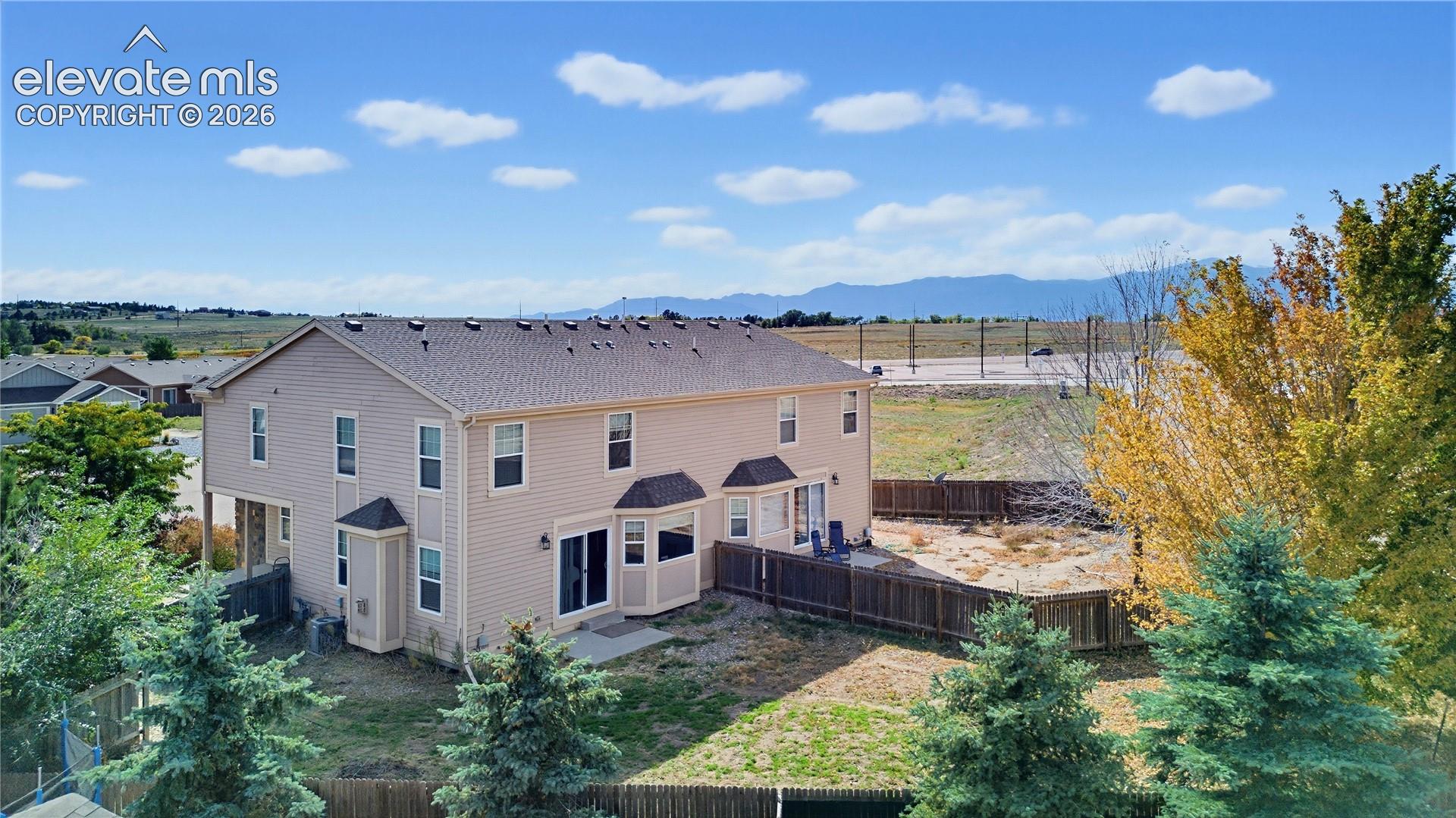Two-story exterior featuring beige siding, a shingled roof, bay windows, and an enclosed backyard with a wood fence and mountain backdrop