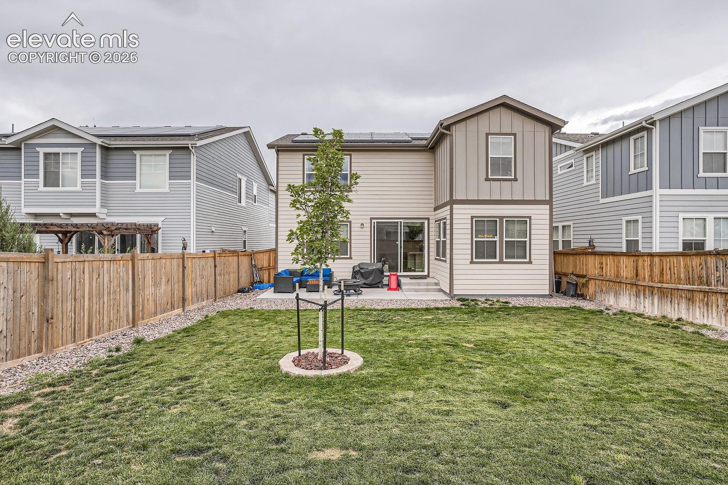 Rear exterior featuring multi-textured siding, solar panels, a concrete patio, wood-style privacy fencing, and a sodded yard