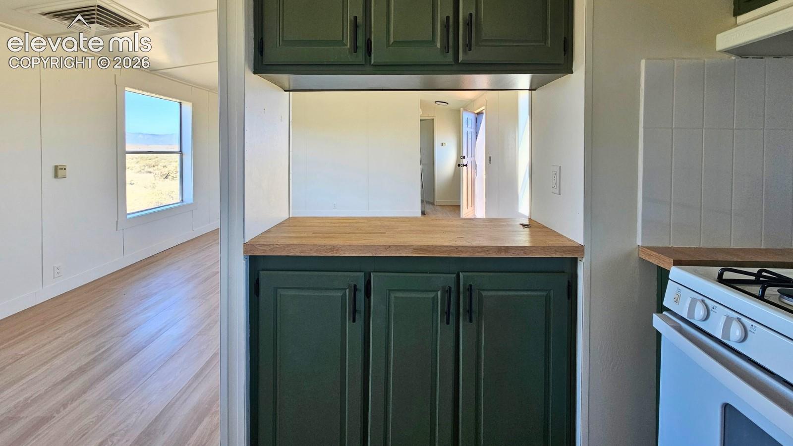 Kitchen featuring green cabinetry, wood-finish countertops, matte black hardware, and light-tone wood-finish flooring