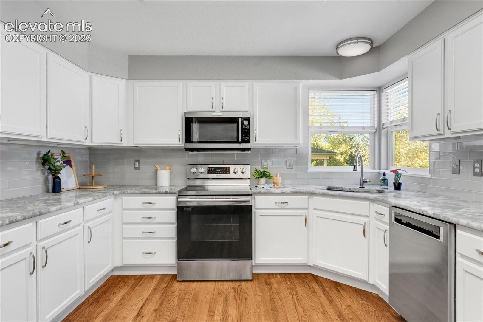 Kitchen featuring white shaker cabinetry, stone-surface countertops, subway tile backsplash, stainless steel appliances, and wood-finish flooring