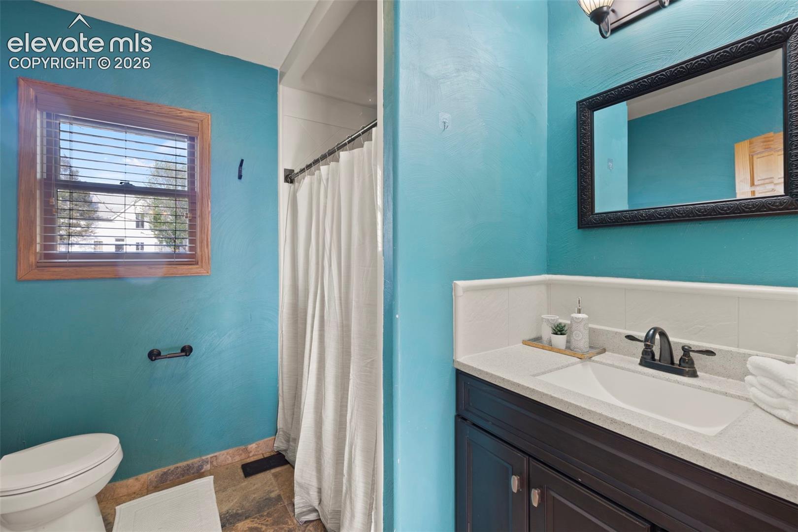 Bathroom featuring a wood-framed window, tile flooring, and a vanity with an undermount sink and dark cabinetry