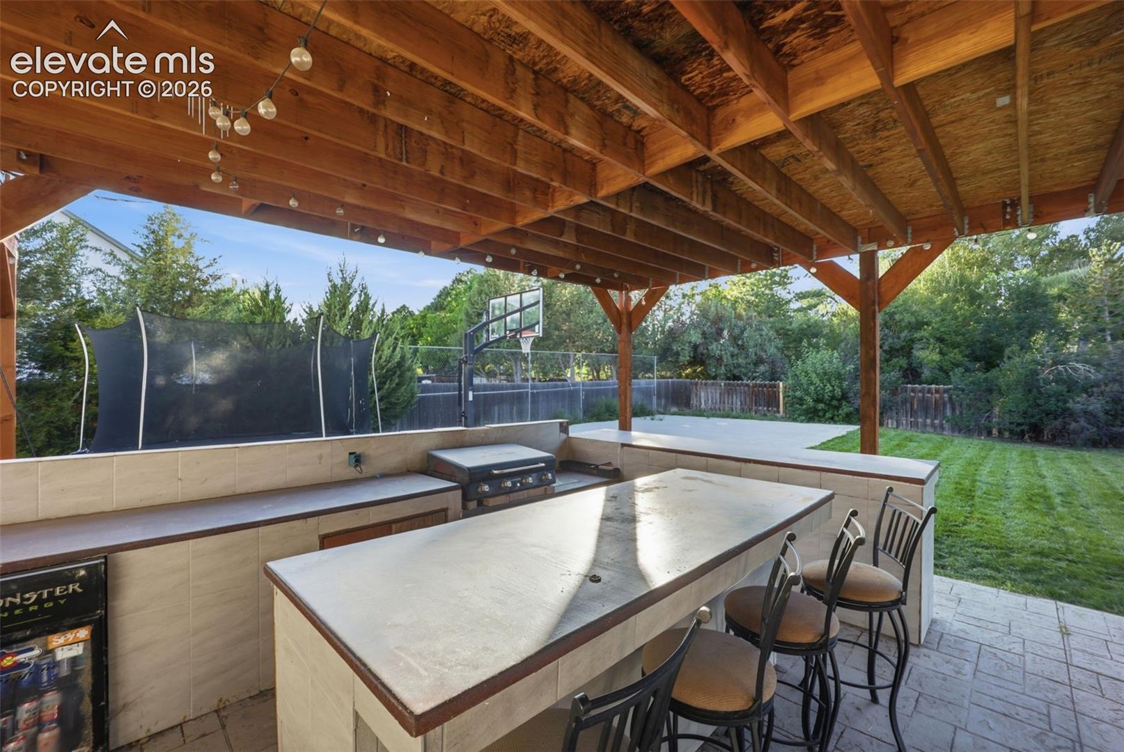 Expansive covered patio featuring a built-in outdoor kitchen with a grill, integrated bar seating, and a concrete paver patio