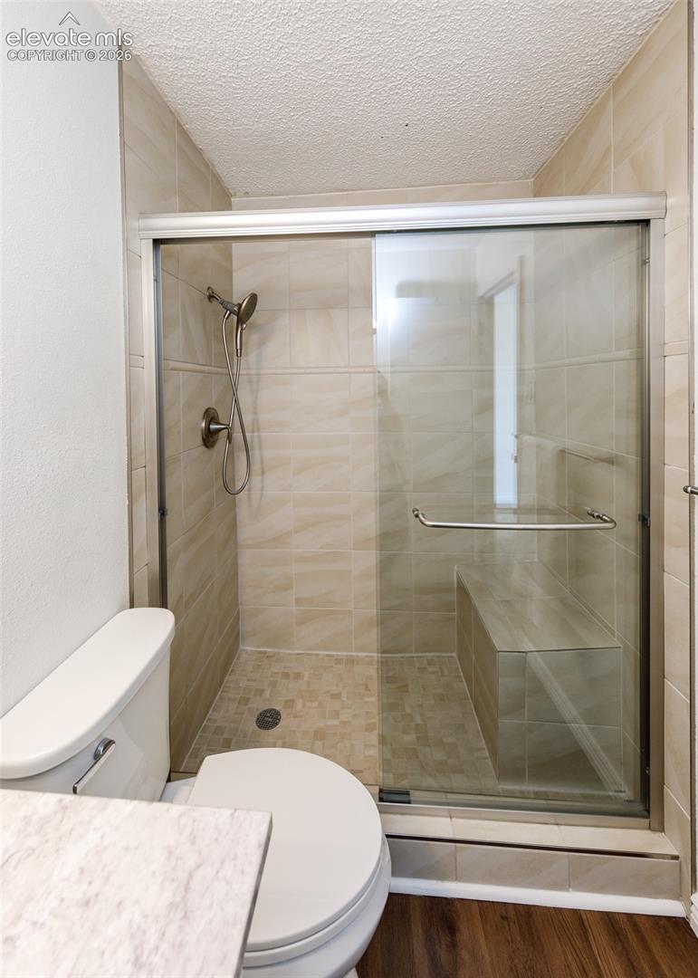 Walk-in shower featuring glass sliding doors, built-in bench seating, neutral-toned tile walls, a mosaic tile floor, and a handheld shower fixture