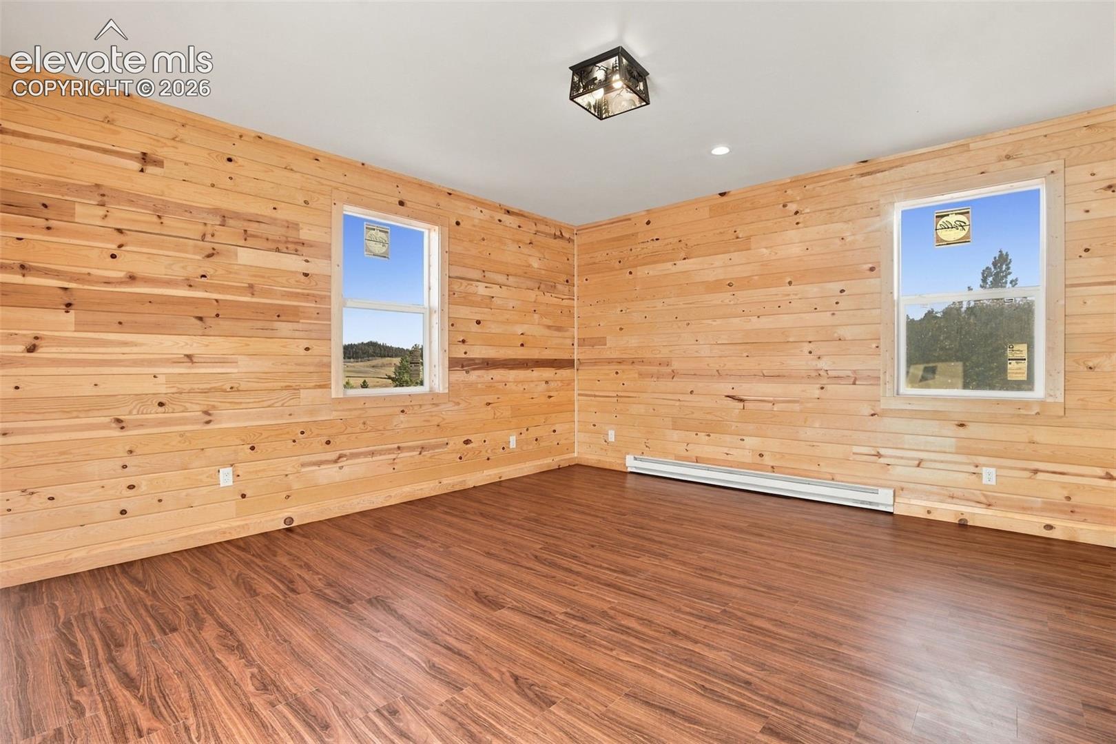 Interior room featuring horizontal wood-plank wall paneling, wood-finish flooring, two double-hung windows, and a box-style ceiling light fixture