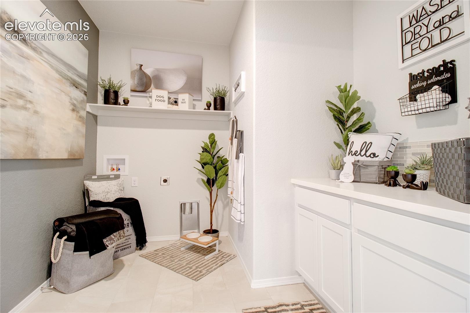 Dedicated laundry area featuring white cabinetry, solid-surface countertops, a floating wall shelf, and tile flooring