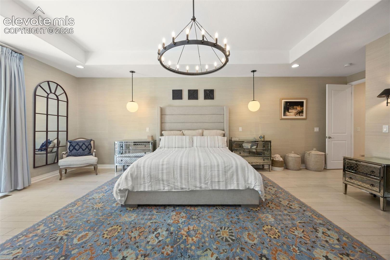 Spacious room featuring light wood-finish flooring, a tray ceiling, and an ornate black chandelier