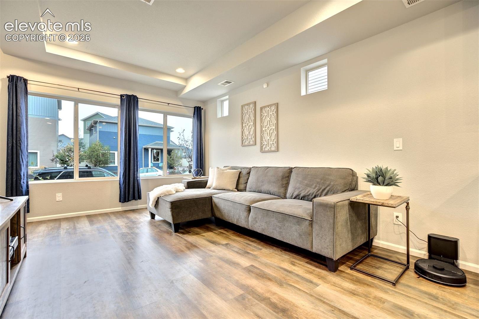 Living area featuring tray ceilings, wood-finish flooring, large picture windows, and dual transom windows