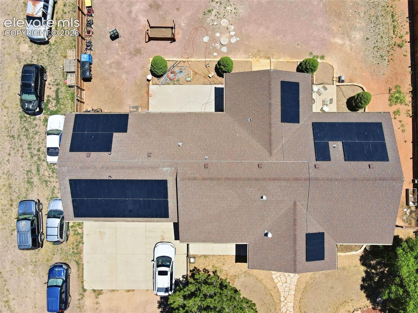 Gable roof home featuring multiple solar panel arrays, a concrete driveway, a rear patio with concrete and stone paver sections, and mature landscaping
