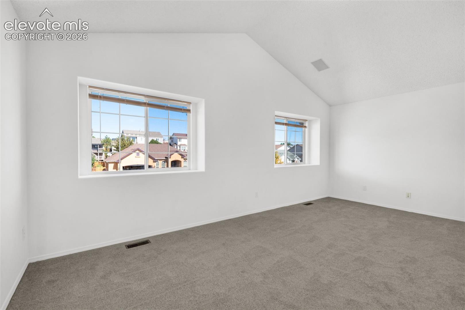 Vaulted ceiling with an integrated speaker system, neutral gray carpeting, and dual windows