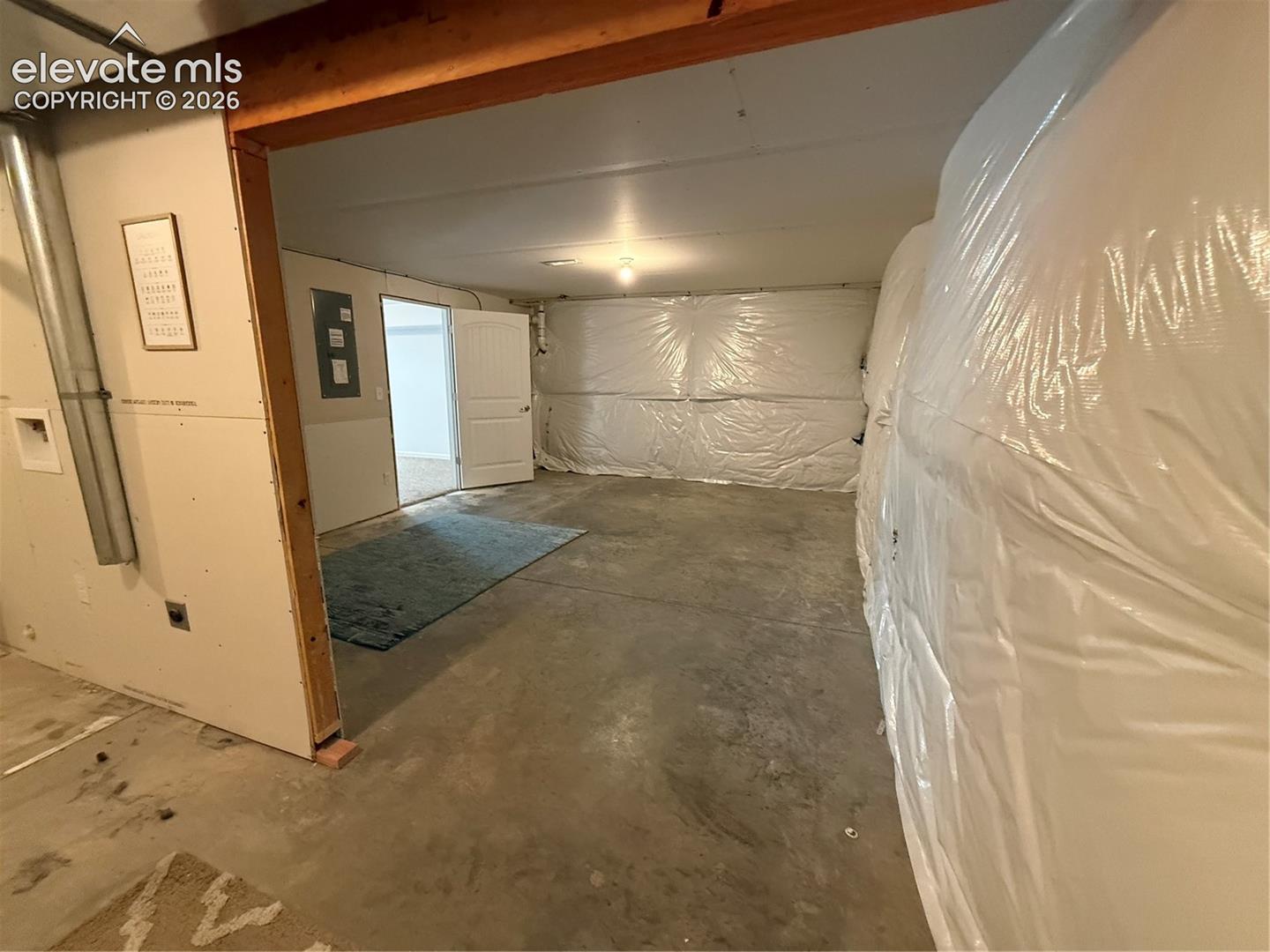 Unfinished lower level featuring concrete flooring, exposed wooden support beams, and perimeter vapor barrier wall treatments