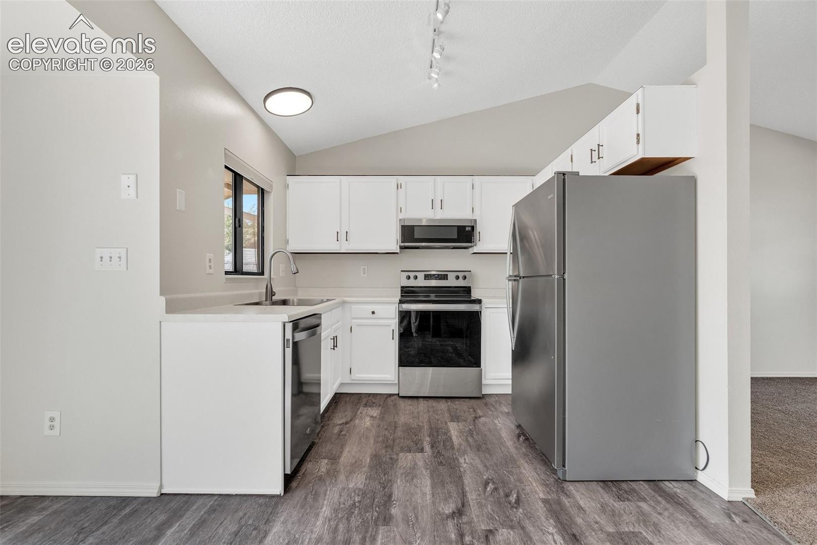 Kitchen featuring stainless steel appliances, white cabinetry, wood-finish flooring, and vaulted ceilings